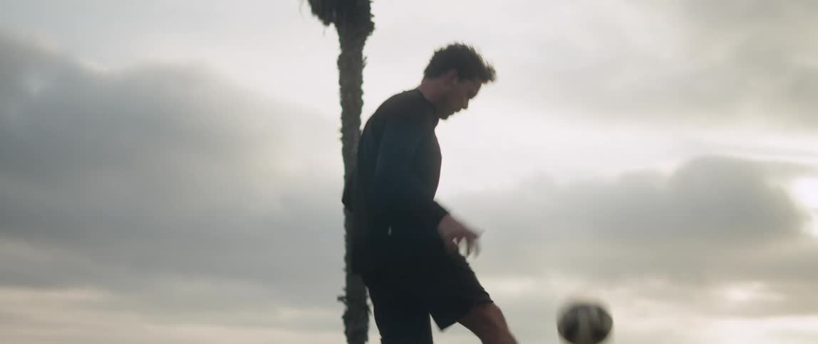 A man is standing outside and bounces a soccer ball off his head and keeps it in the air using his feet and knees