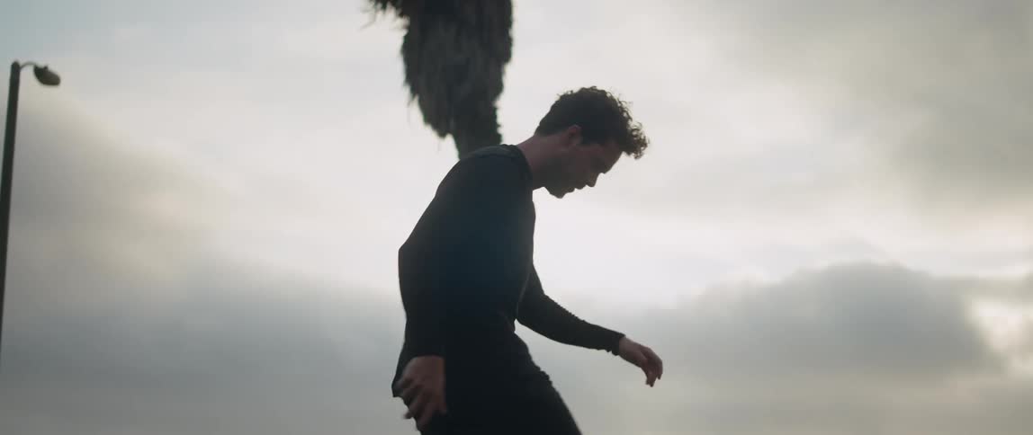 A man is standing outside bouncing a soccer ball into the air using his feet
