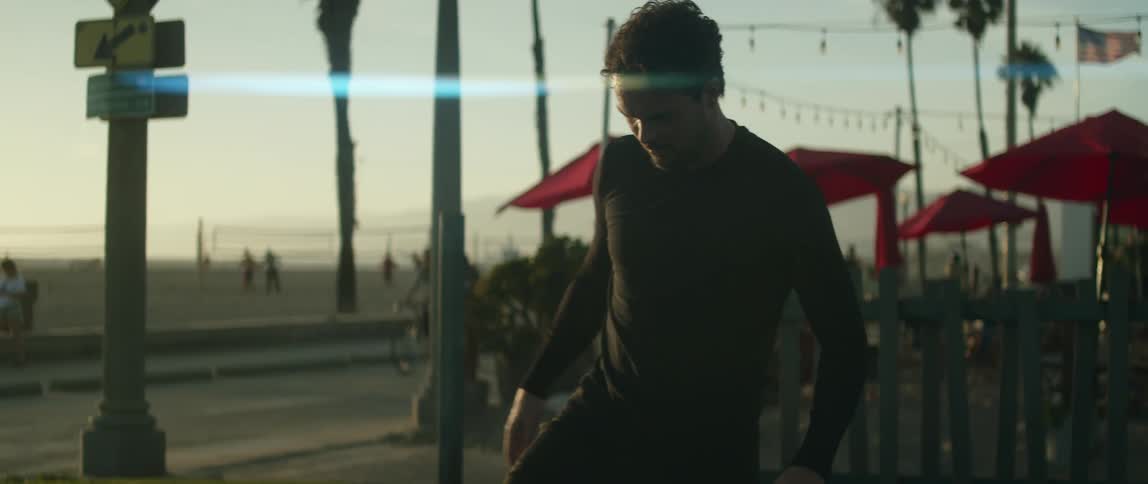 Man plays with soccer ball as cyclists pedal along road between him and the beach