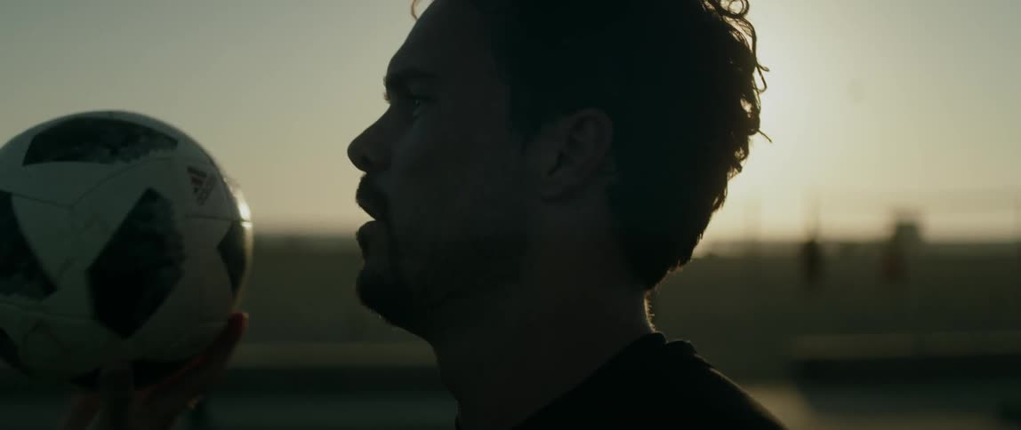 Man wearing a black sweatshirt spins a football on his finger near the beach at sunset