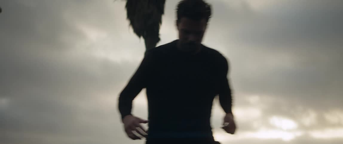 A man kicking around a soccer ball near a silhouetted palm tree at sunset