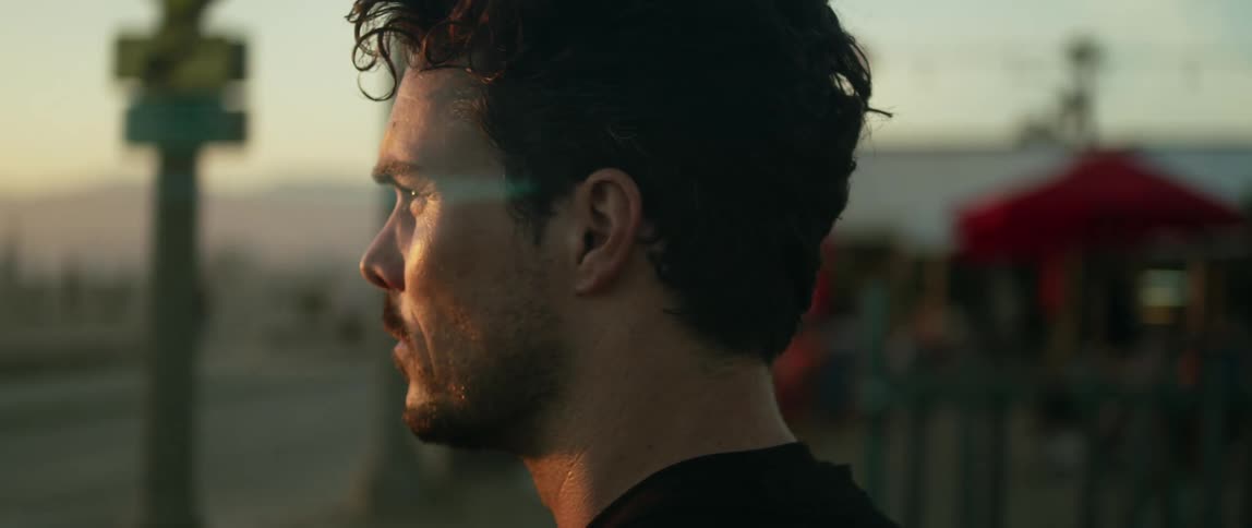 Young man standing on a park near a beach looks at the horizon at sunset