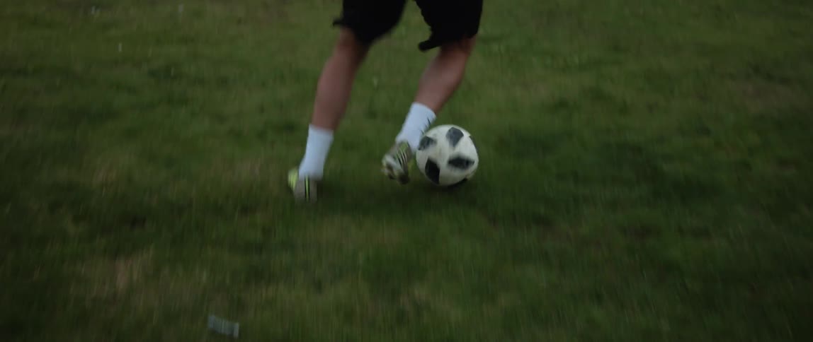 Close up of the legs of a man practicing with a soccer ball on a field at daytime