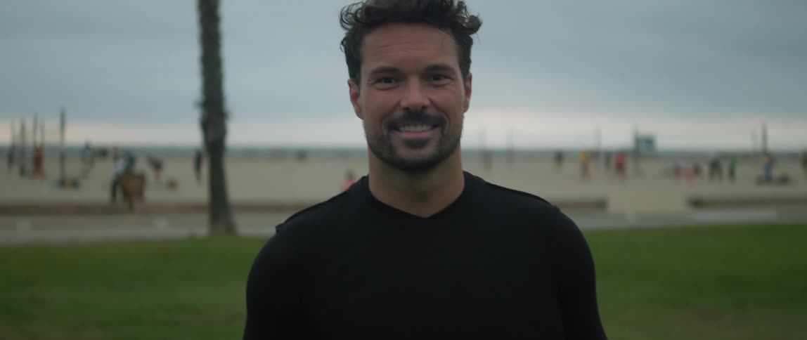 A man is standing in a field holding a soccer ball as he looks ahead and smiles