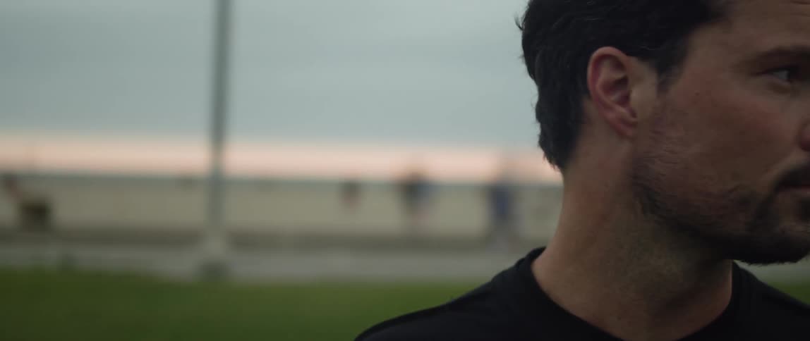 Man standing in park looks around at building and a fitness class
