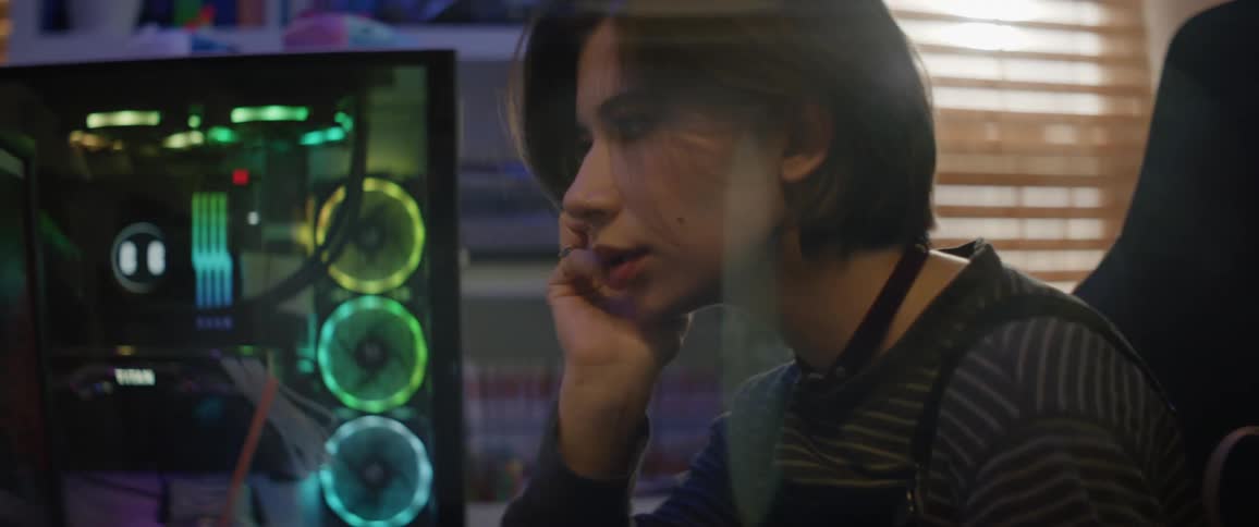 A teenage girl is sitting in front of a gaming computer playing a video game