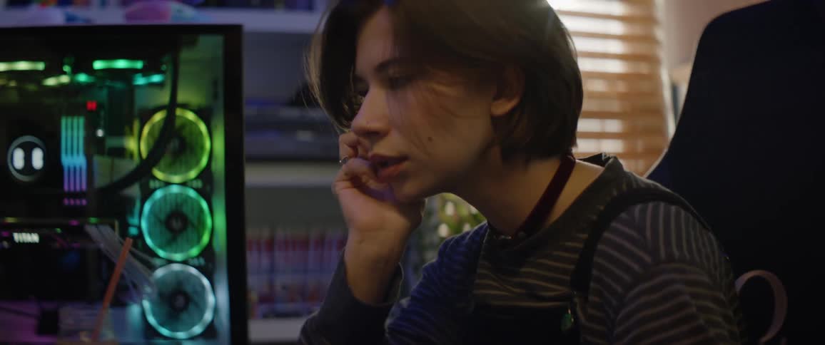 A teenage girl is sitting in front of a gaming computer playing a video game