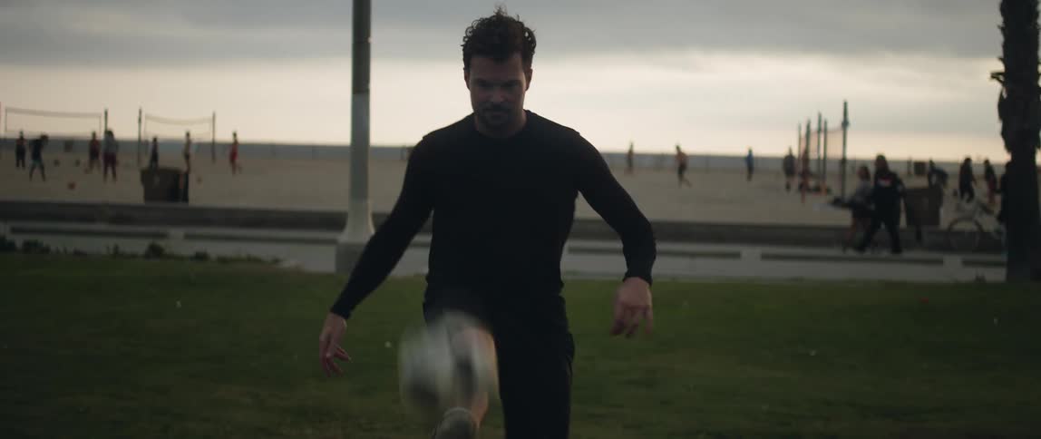 Man with black sweatshirt and shorts juggles a soccer ball near the beach
