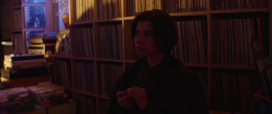 A teenage girl is standing in a room in front of shelves and swaying her head as she gets into the music
