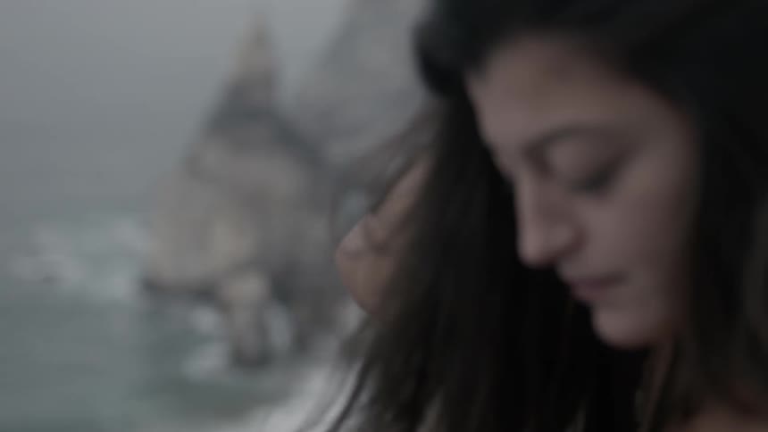 A woman brushes her hair back as she stands on an oceanside cliff