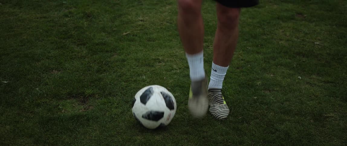 A man is standing in a field moving a soccer ball around with his feet