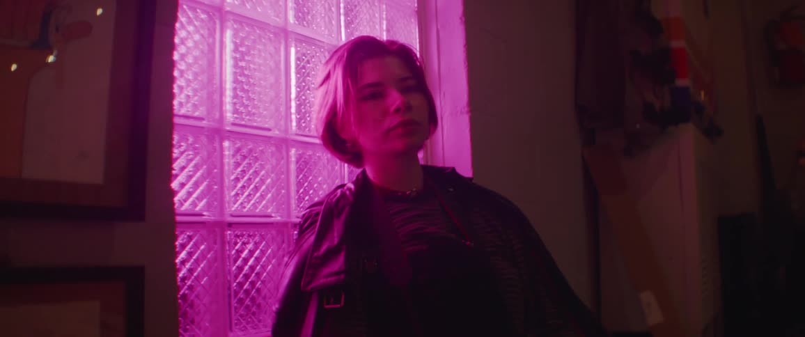 A woman rests against a window as colorful lights flash on the other side of it