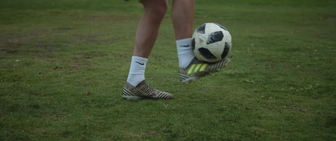 A man is standing in a field and he catches a soccer ball with his foot