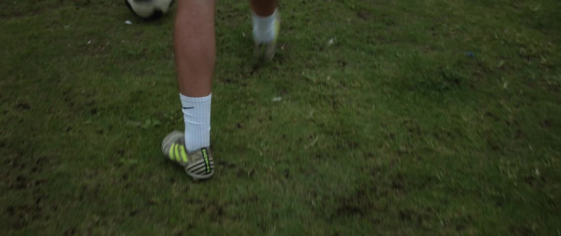 Man wearing black shorts white socks and football boots plays soccer on green grass