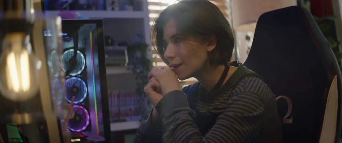 A teenage girl is sitting in front of a gaming computer playing a video game