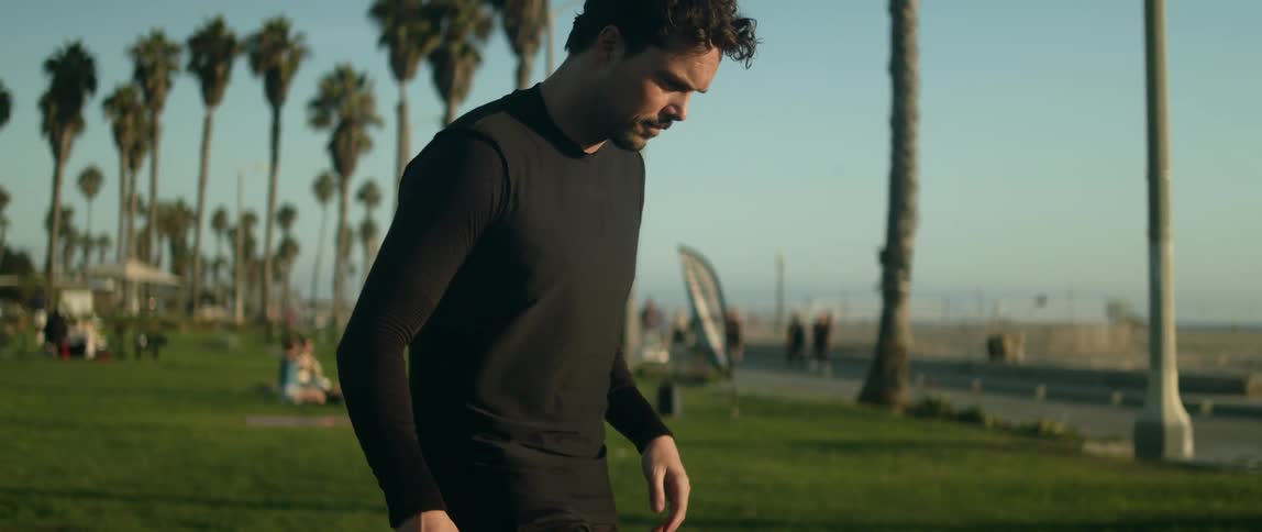 Man plays with soccer ball in busy park across a road from the beach