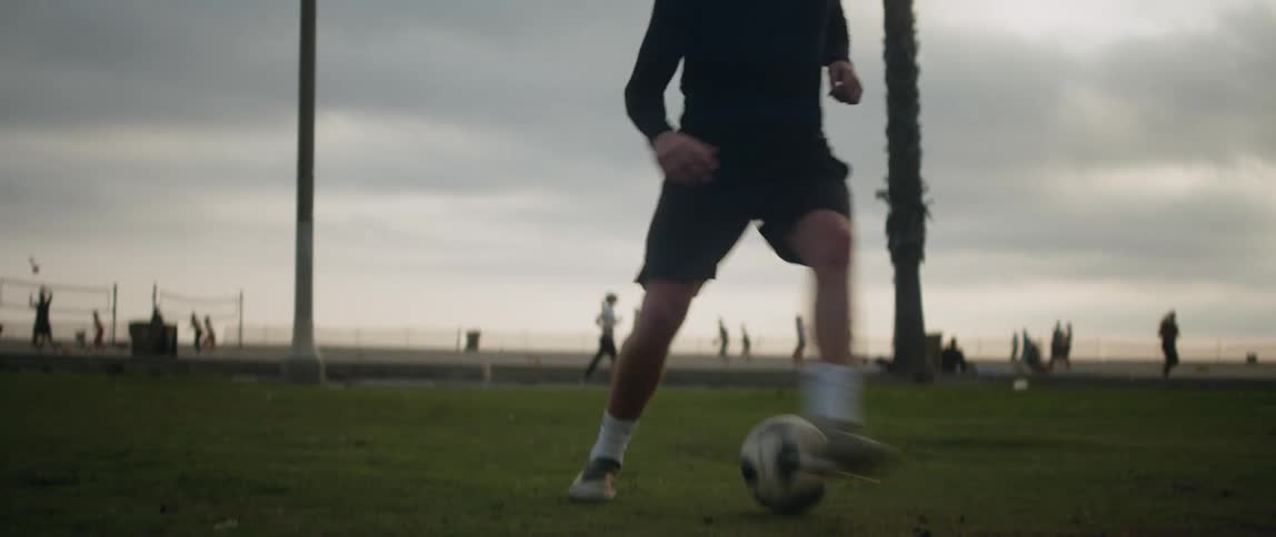 Man dribbles soccer ball in park near volleyball courts
