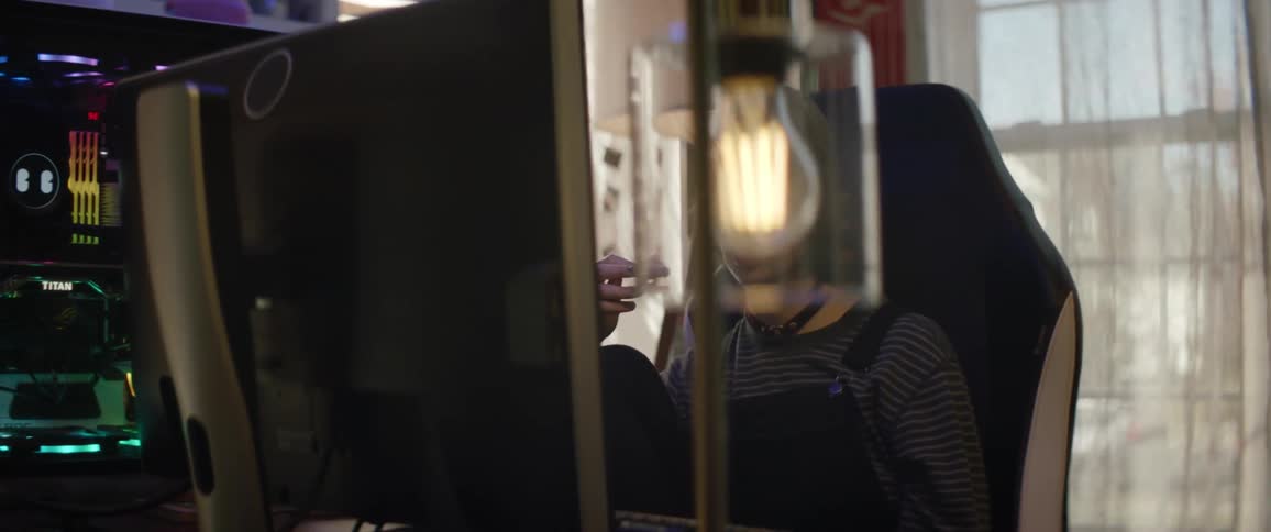 A teenage girl sitting in front of a desktop computer while deep in thought