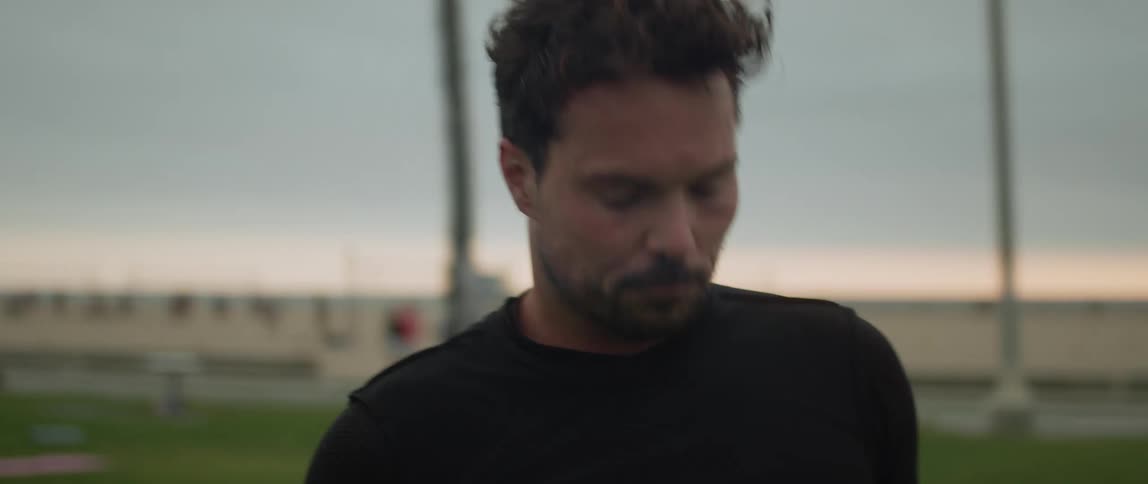 A man is outside at a beach wiping sweat off his face