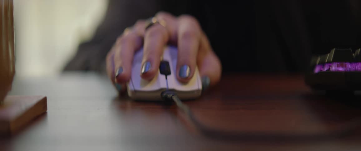 A teenage girl is sitting at a desk with her hand on a computer mouse as she moves it across the surface