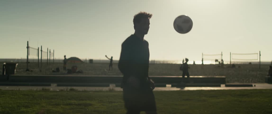 A man juggles a soccer ball with his legs on a beach during the day