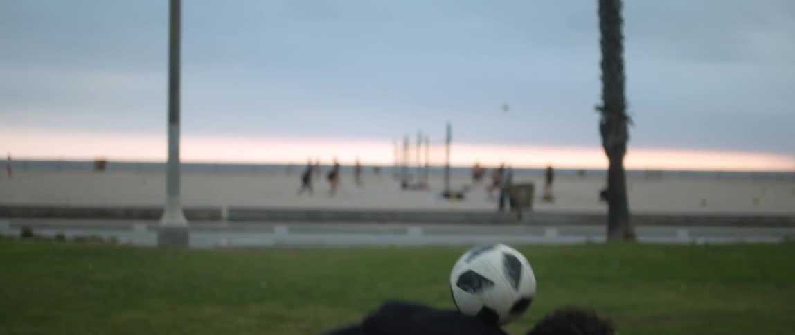 A man tosses a ball up in the air catching it on the back of his neck as he practices near the beach