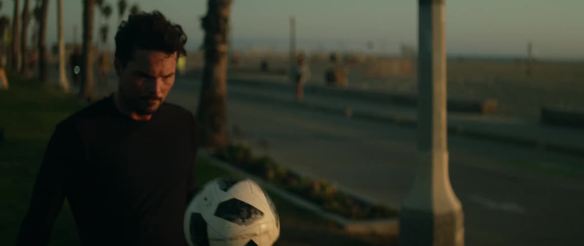 Man practices with soccer ball in park near busy road across from beach