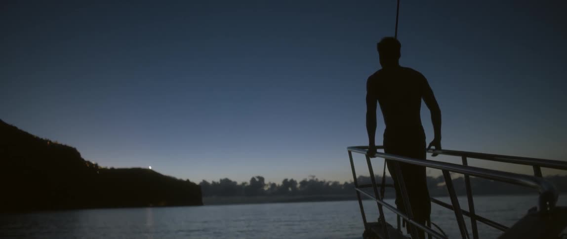 Man standing at the front of a ship holding onto the ship's railing
