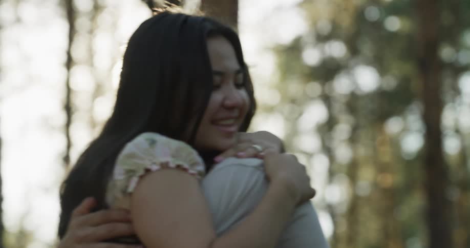 A man and a woman are hugging each other as the sun shines through the trees in the woods