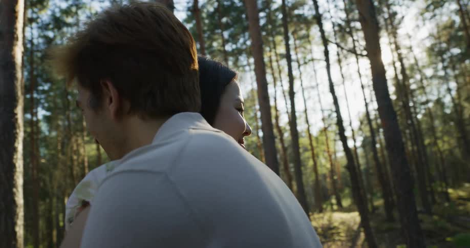 Couple smile while hugging each other and swaying in woods on sunny day