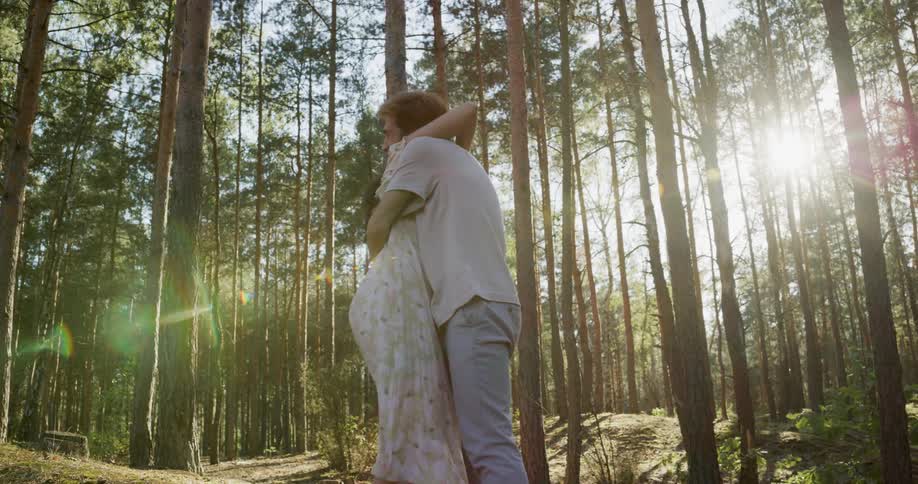 Man wearing white shirt and jeans proposes woman in white floral dress in the dense deciduous forest