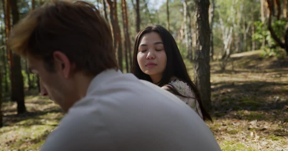 A teenage couple sit next to each other in the woods and stay silent showing possible tension