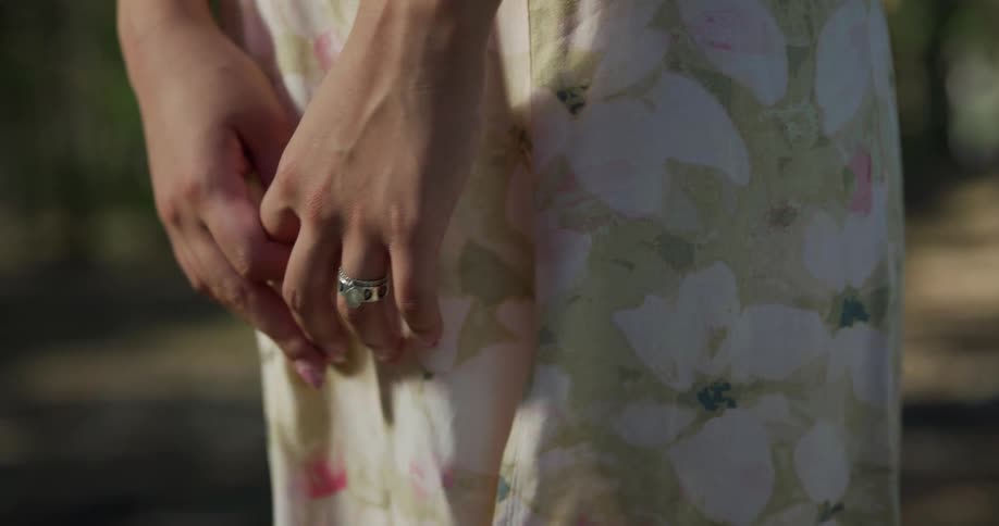Woman wearing skirt and ring stands in woods on windy day clasping her hands together
