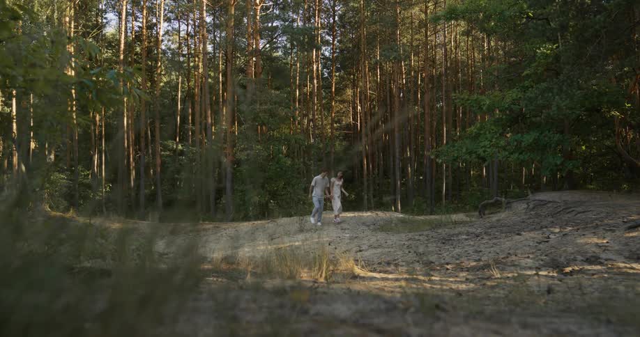 A couple holds hands as they walk in a clearing in the forest