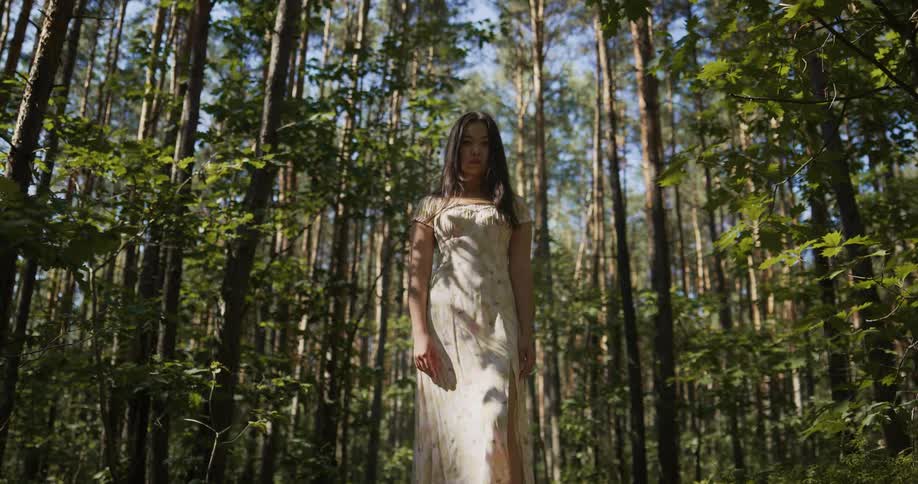A woman wearing a dress is standing in a forest on a sunny day