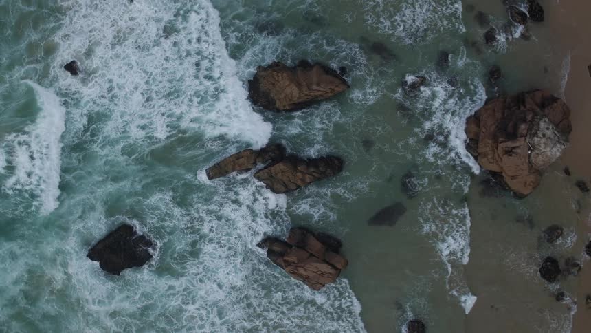 Waves crash against rock formations and onto a beach during daylight
