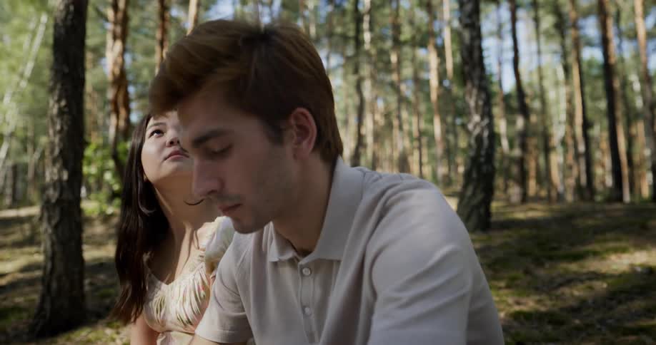 A man and a woman are sitting together in the woods as the sun shines through the trees