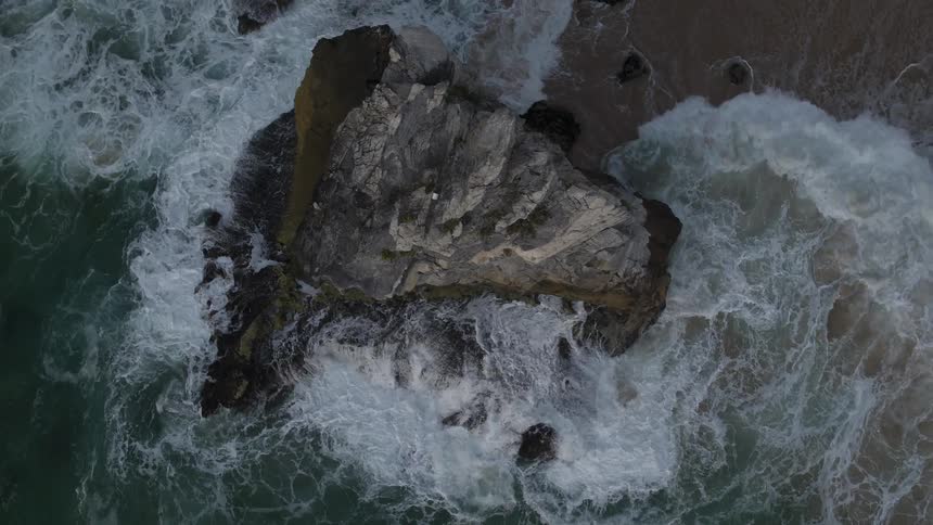 Waves crash against a tall rock formation and onto the beach