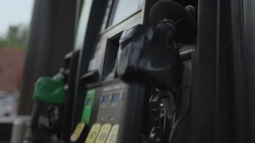 Gas pump nozzles sit in position on the pump as a man is walking in the distance