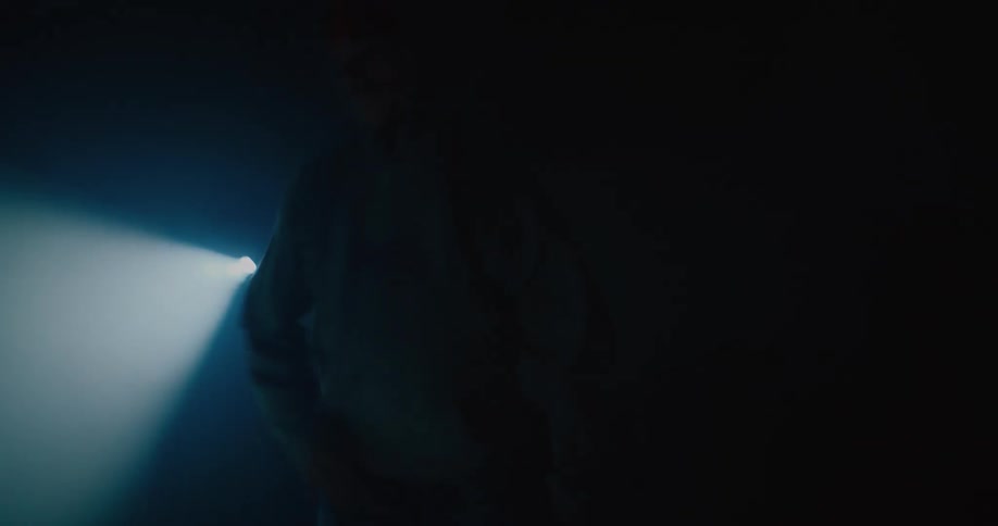 A spotlight shines over a man as he breakdances in a dark room