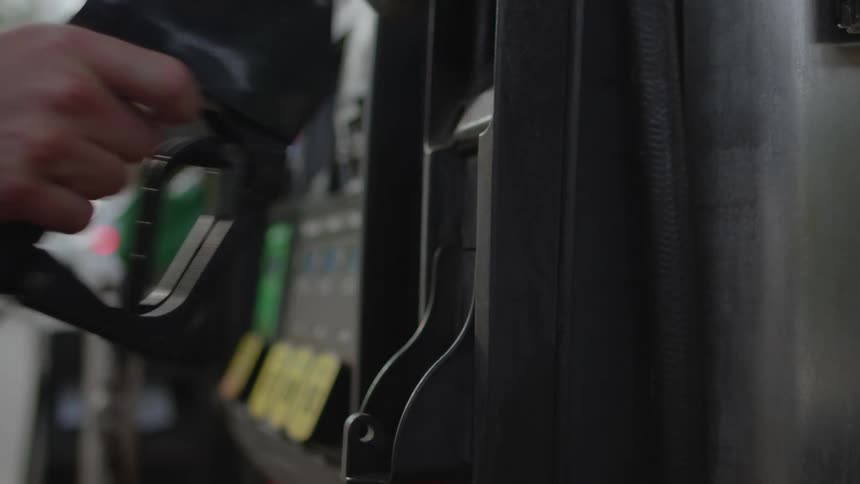 A man standing near a gas pump reaches for the fuel nozzle as he pushes a button to select his gas