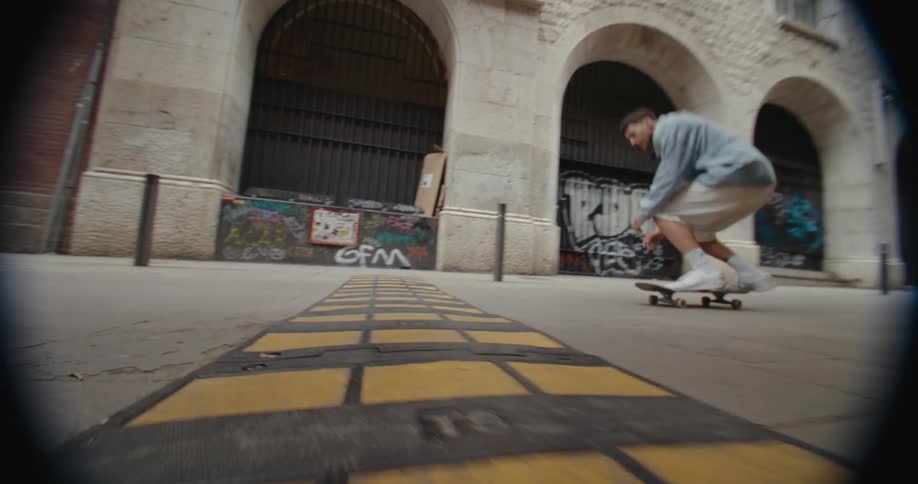 A man skateboarding on a city sidewalk jumps over a large bump