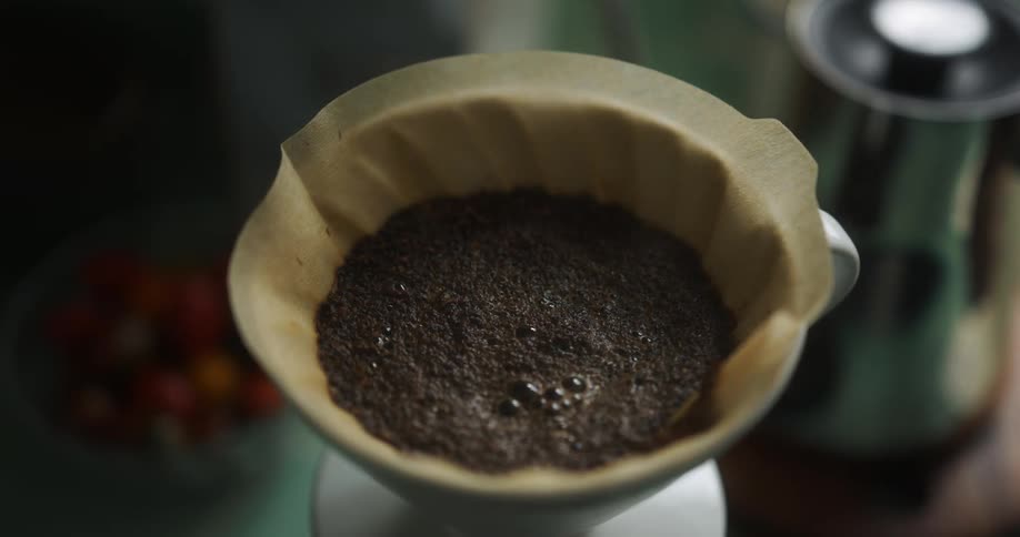 Someone pours hot water into a coffee filter filled with ground coffee and sets the pot down
