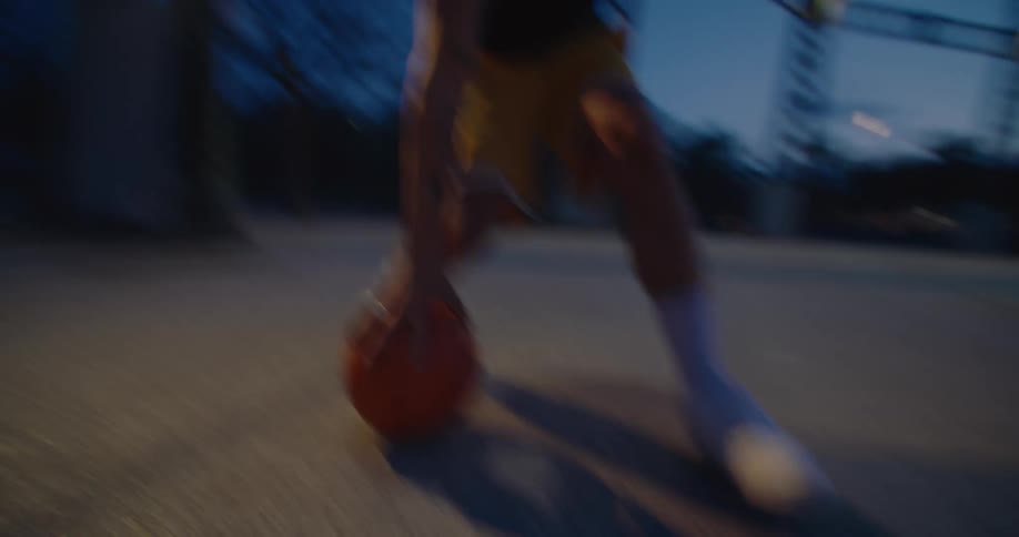 A man is outside in a park dribbling a basketball under a clear blue sky