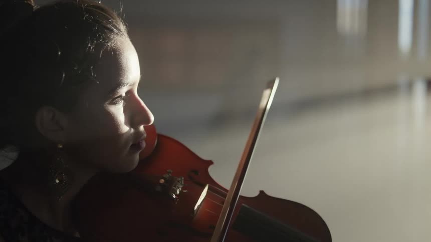 Close up of female musician wearing earrings play violin while the sunlight streams through window