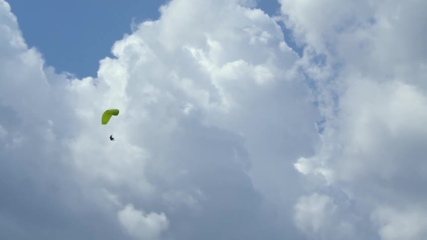 A paraglider descends through the sky with a yellow canopy