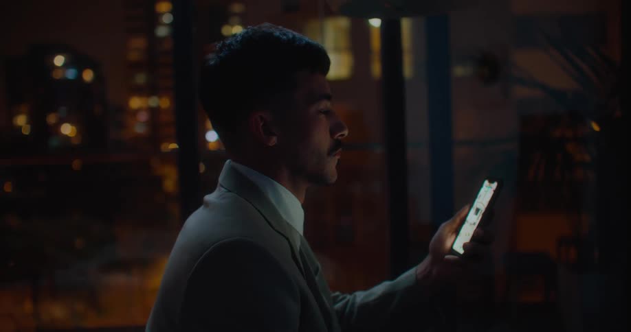 A man leans back onto his bed while reading text messages on his phone