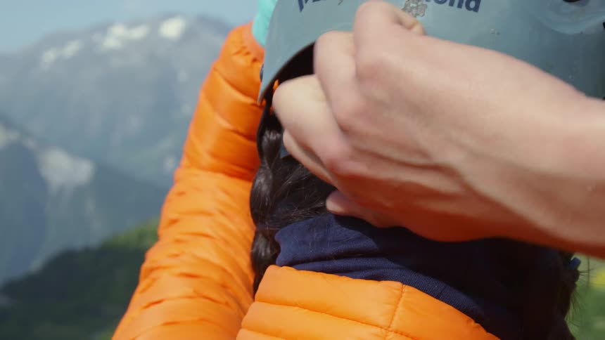 A woman adjusts her helmet as she stands looking at the mountains