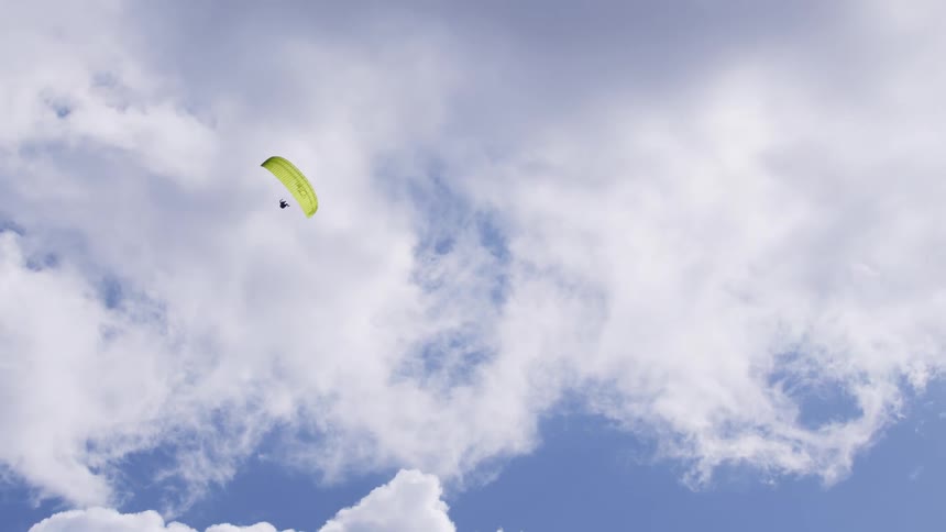 A paraglider sails across a cloudy sky