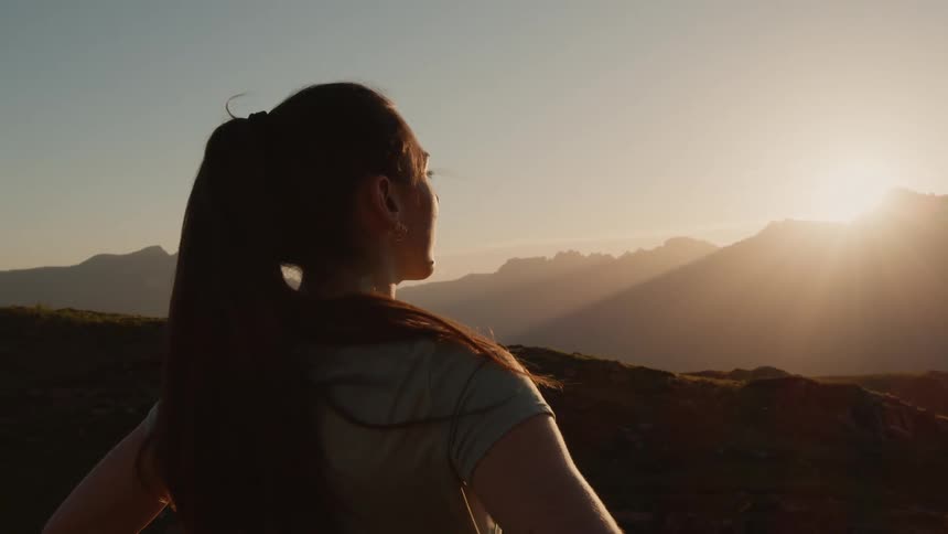 A woman stands and looks out at a mountain range